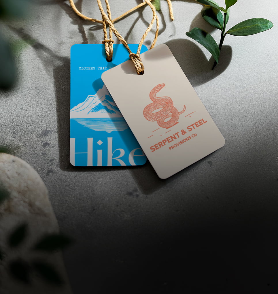 Two printed swing tags on a concrete surface with greenery, showcasing custom branding and high-quality print, ideal for retail packaging.