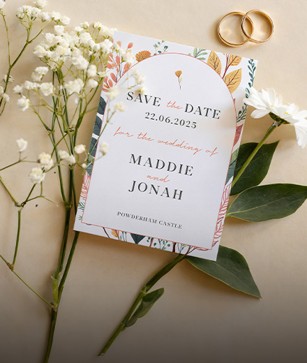 A save the date card for a wedding delicately placed amidst flowers and wedding rings, creating a charming and romantic scene.