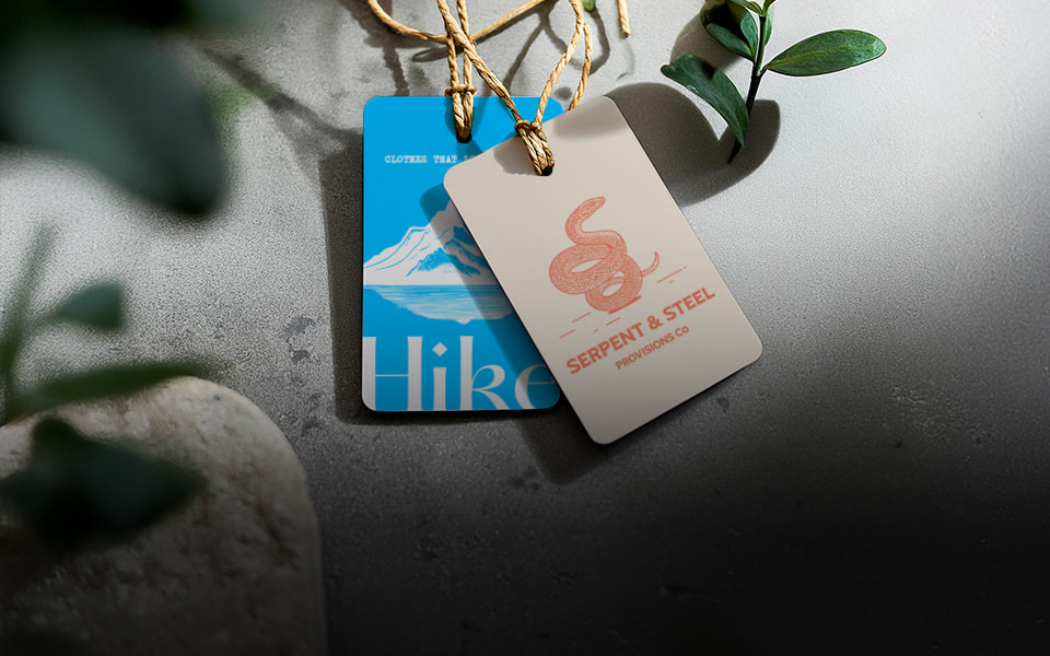 Two printed swing tags on a concrete surface with greenery, showcasing custom branding and high-quality print, ideal for retail packaging.