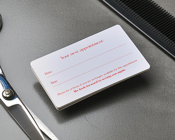 An appointment card for a barber shop placed on a table next to a pair of scissors and a comb.