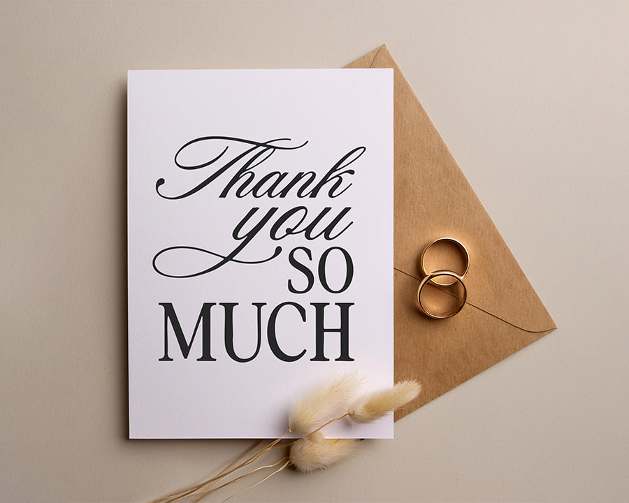 Elegant wedding thank you card with bold black text, placed next to a brown kraft envelope and wedding rings, ideal for couples seeking stylish, impactful thank you cards.